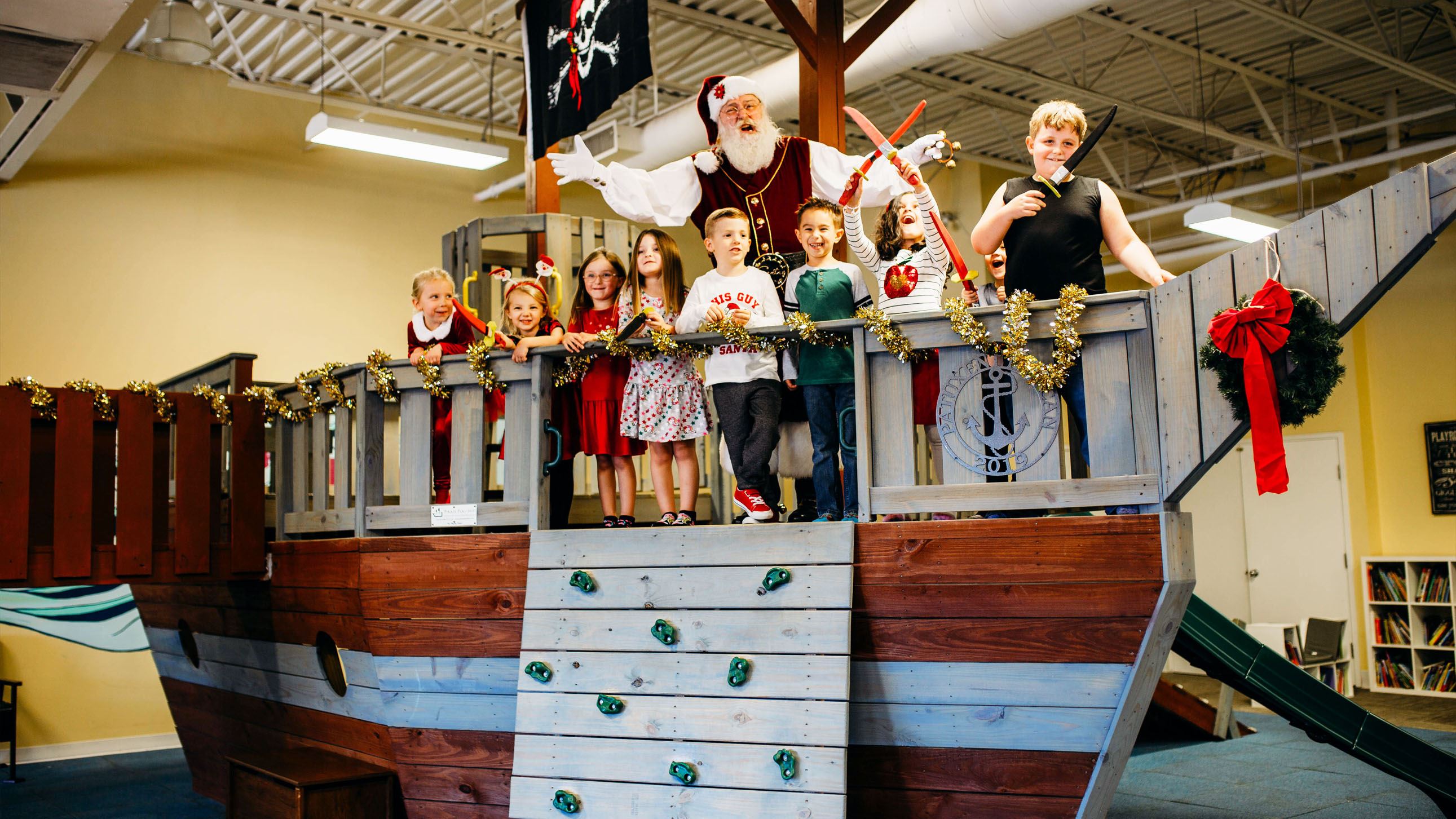 Santa Claus surrounded by children standing on a pirate ship indoor playground