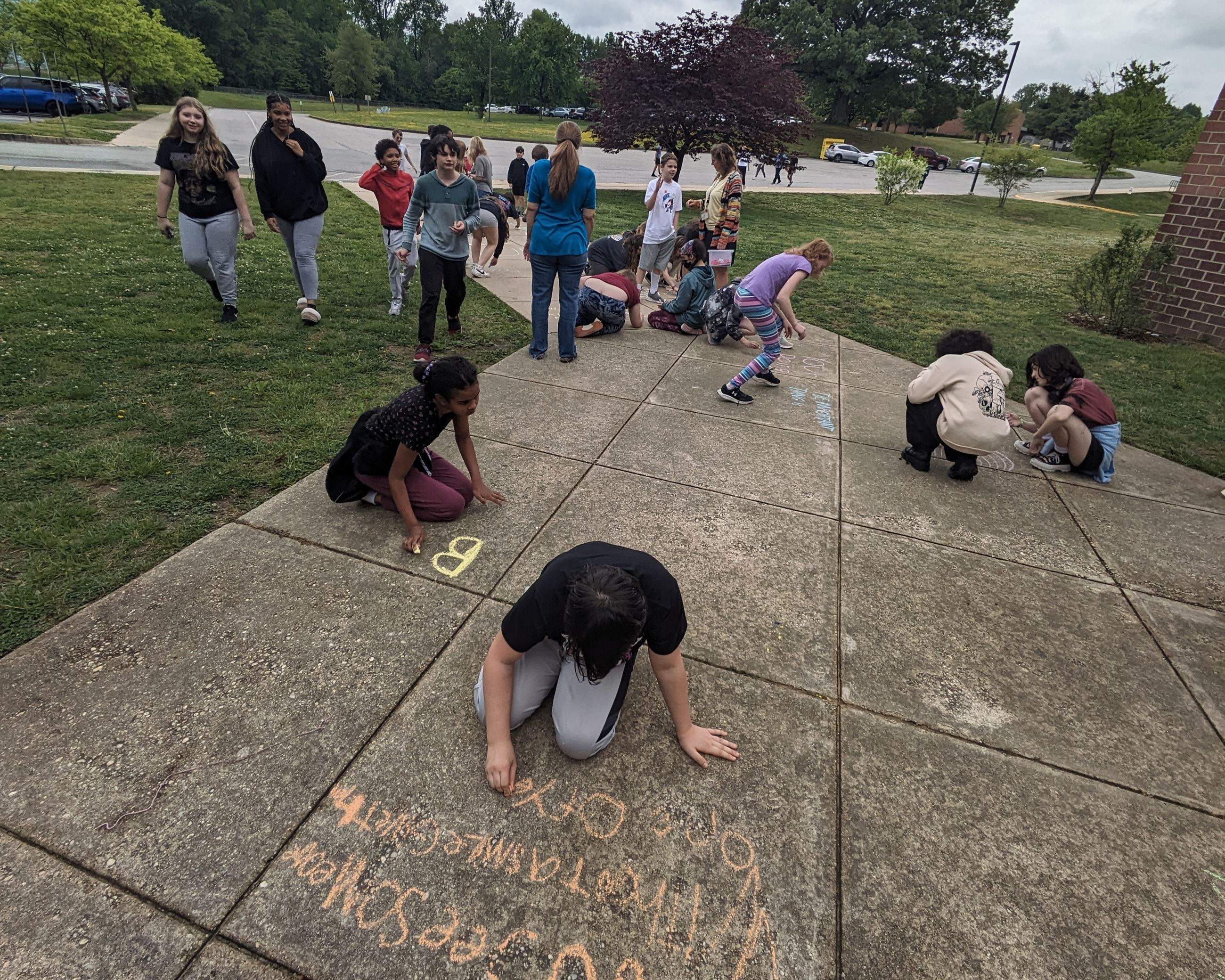 A large group of kids drawing with chalk on the sidewalk in front of Windy Hill Middle School.