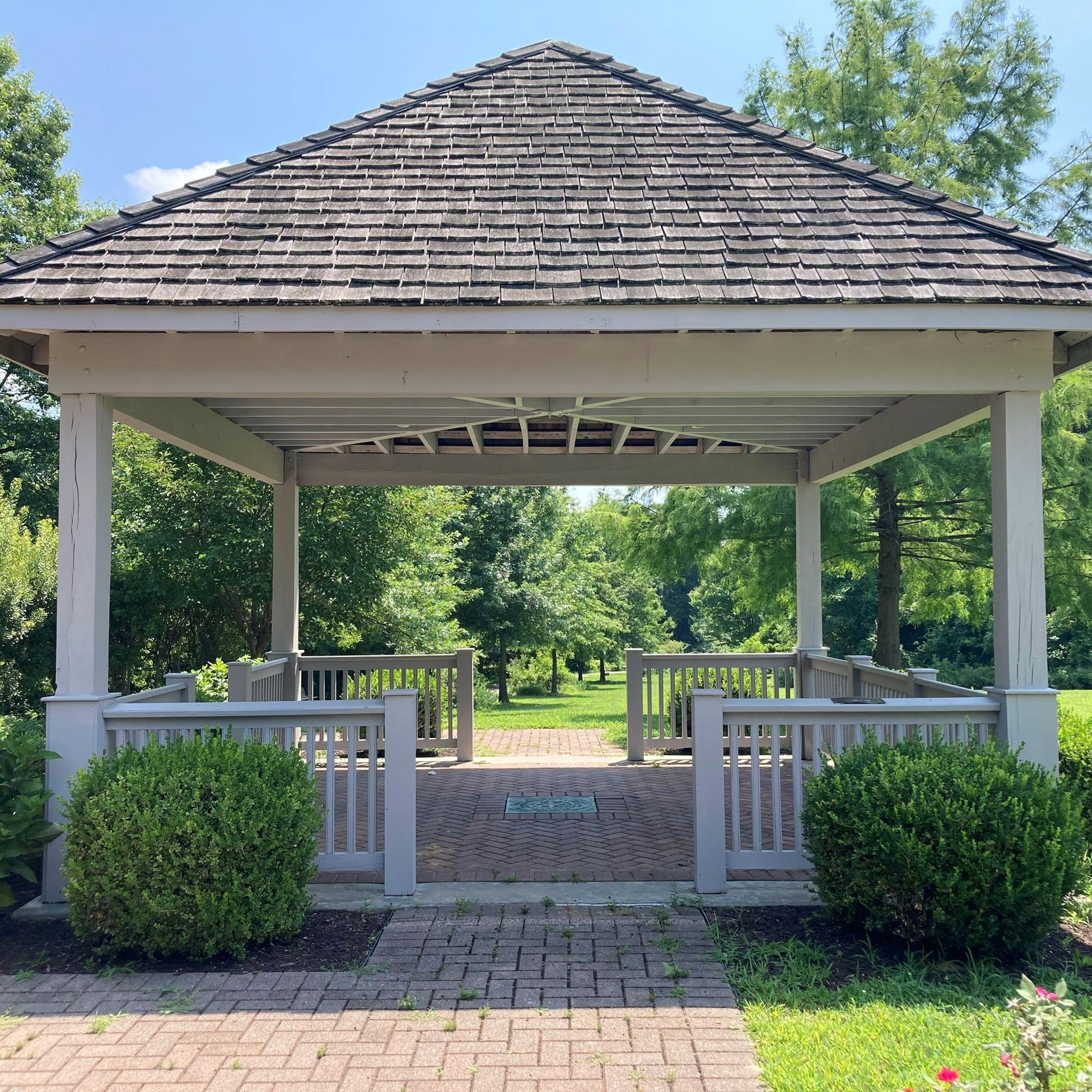 white wooden gazebo surrounded by bushes at a park
